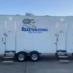 White trailer with two doors and Reel Solutions logo, parked outside.